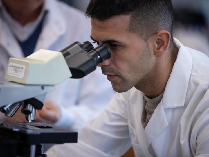 A student wears lab coat and looks into microscope